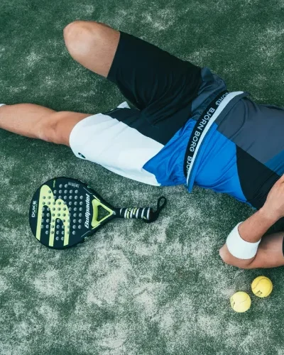 man ligt op de grond met een padel racket en draagt tenniskleding